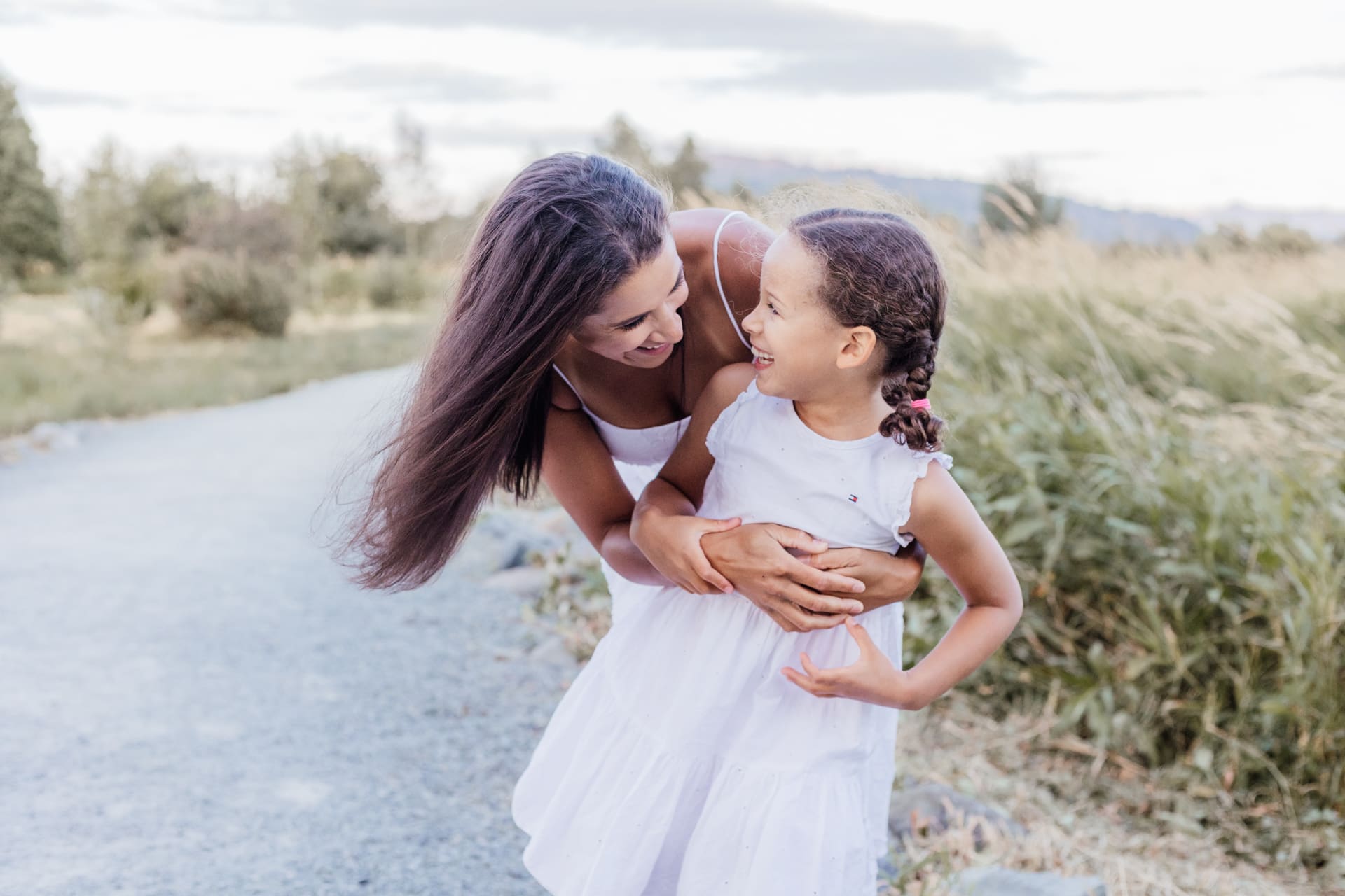 Mother hugging and tickling daughter while laughing — candid family portrait at sunset with Meliza Orellana Photography