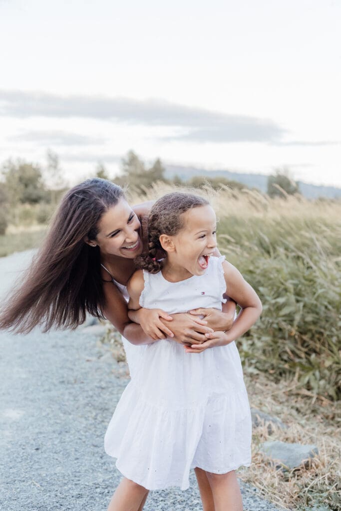 Mother and daughter sharing a close laugh in tall grass — natural light family photography in Maple Ridge.