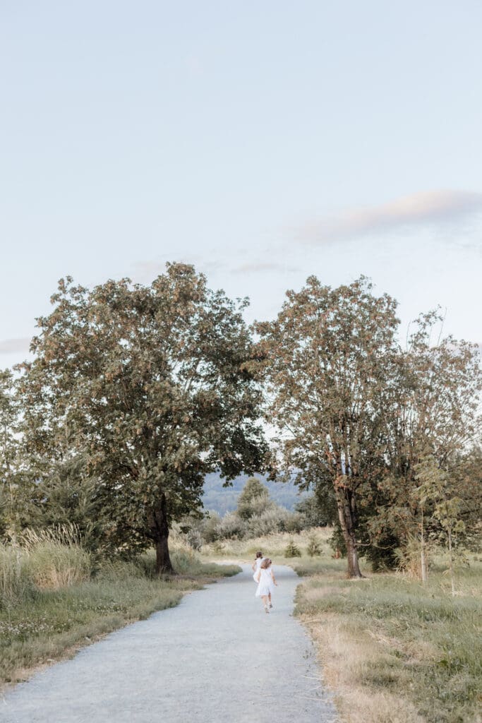 sisters walking down a gravel path surrounded by tall grass during sunset — outdoor family photo by Maple Ridge family photographer Meliza Orellana Photography