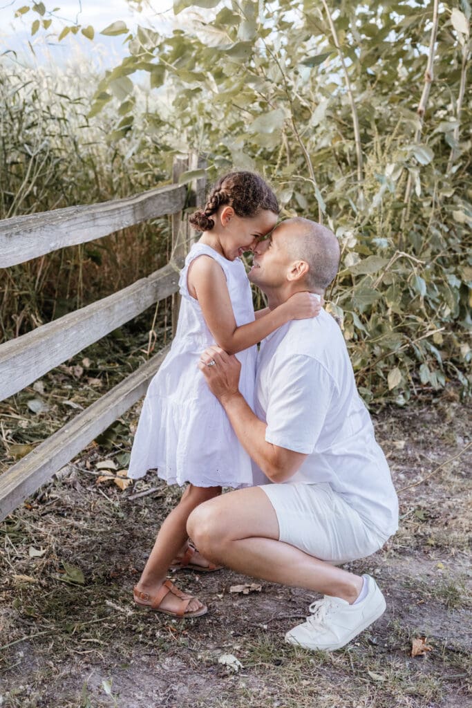 Father kneeling and embracing daughter near wooden fence — candid family connection moment captured at Maple Ridge park