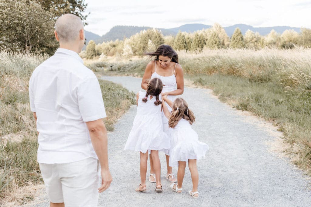 Family of four walking hand in hand down a path, parents in white with two daughters in matching dresses — relaxed family session