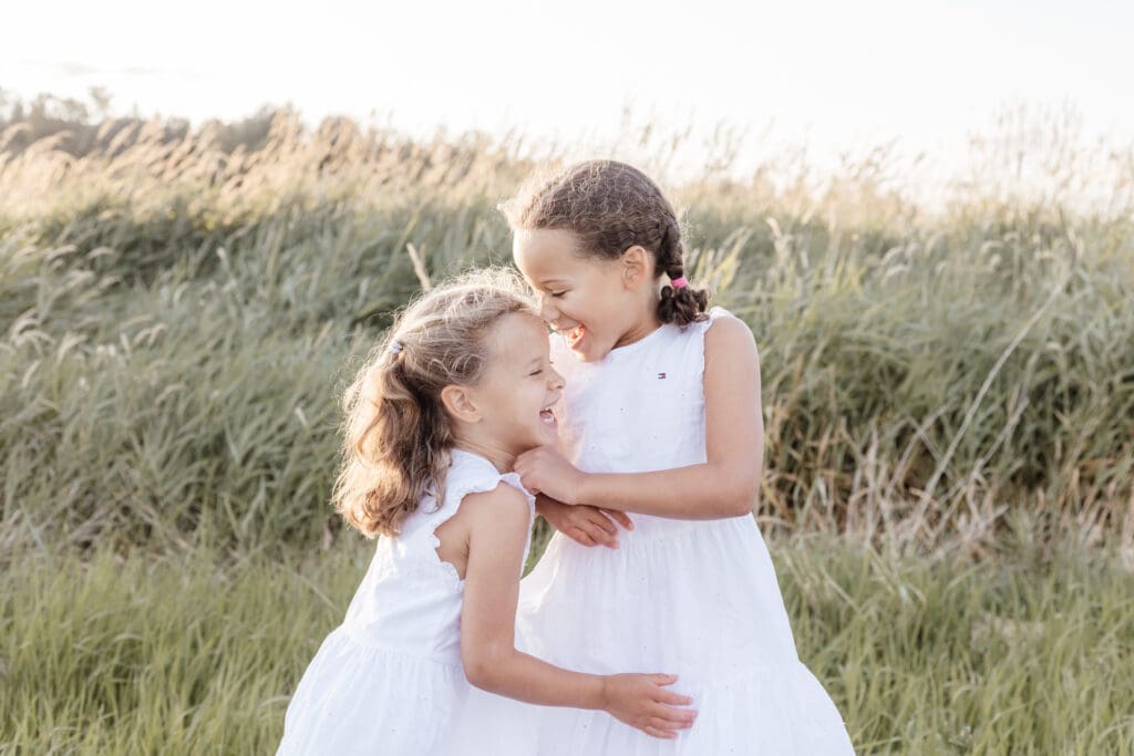 Two young sisters hugging and smiling in golden light — natural outdoor children’s portrait by Maple Ridge photographer Meliza Orellana in Abbotsford Willband Creek Park