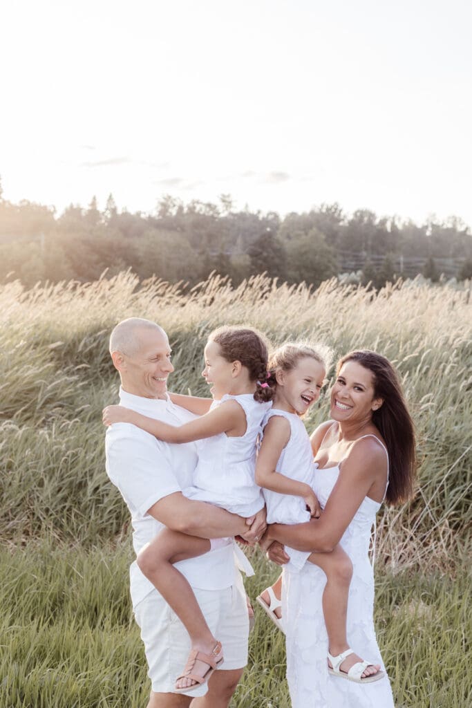 Parents holding two young daughters, all laughing together in evening light — joyful family photo session in Willband Creek Park Abbotsford