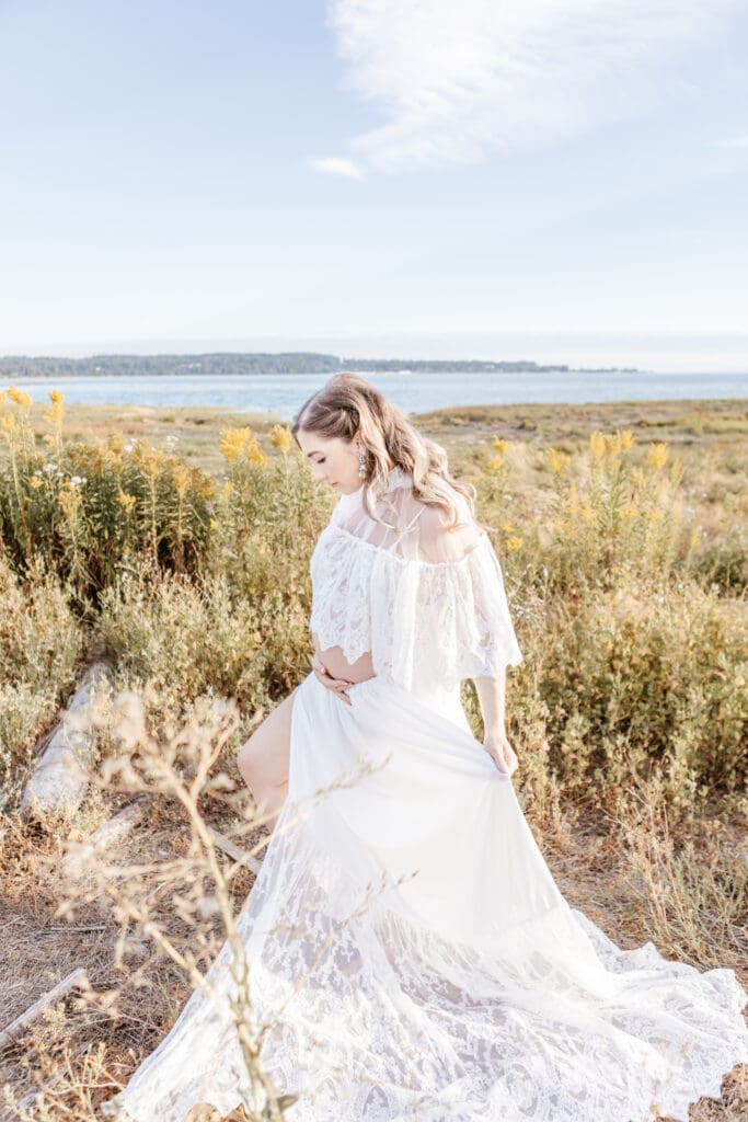 Pregnant woman wearing a flowing white dress during an outdoor maternity session near the water in Surrey at Mud Bay Park