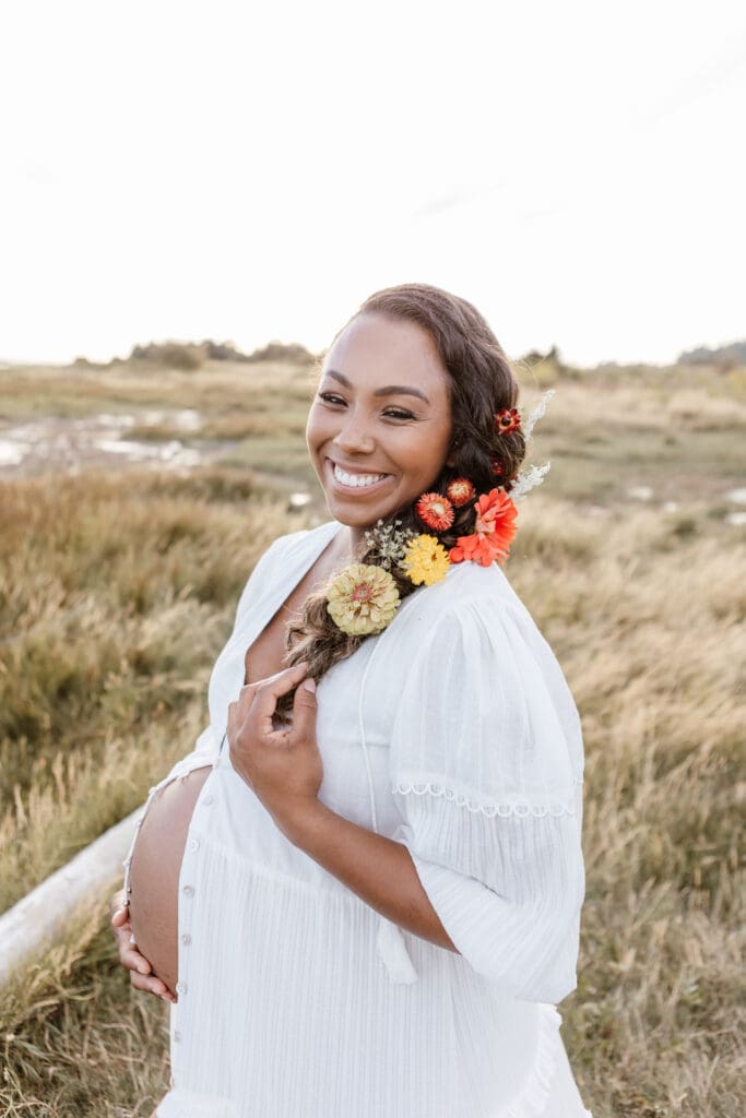 Maternity photo of a woman in a white dress with flowers in her hair standing in a natural field in Surrey at Mud Bay Park