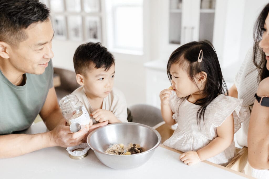 Parents helping their children mix ingredients in a bowl at the counter.