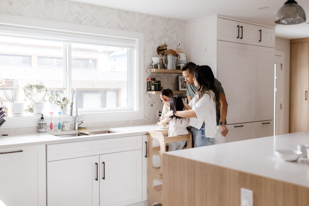 Parents leaning over the kitchen counter guiding their children as they bake.