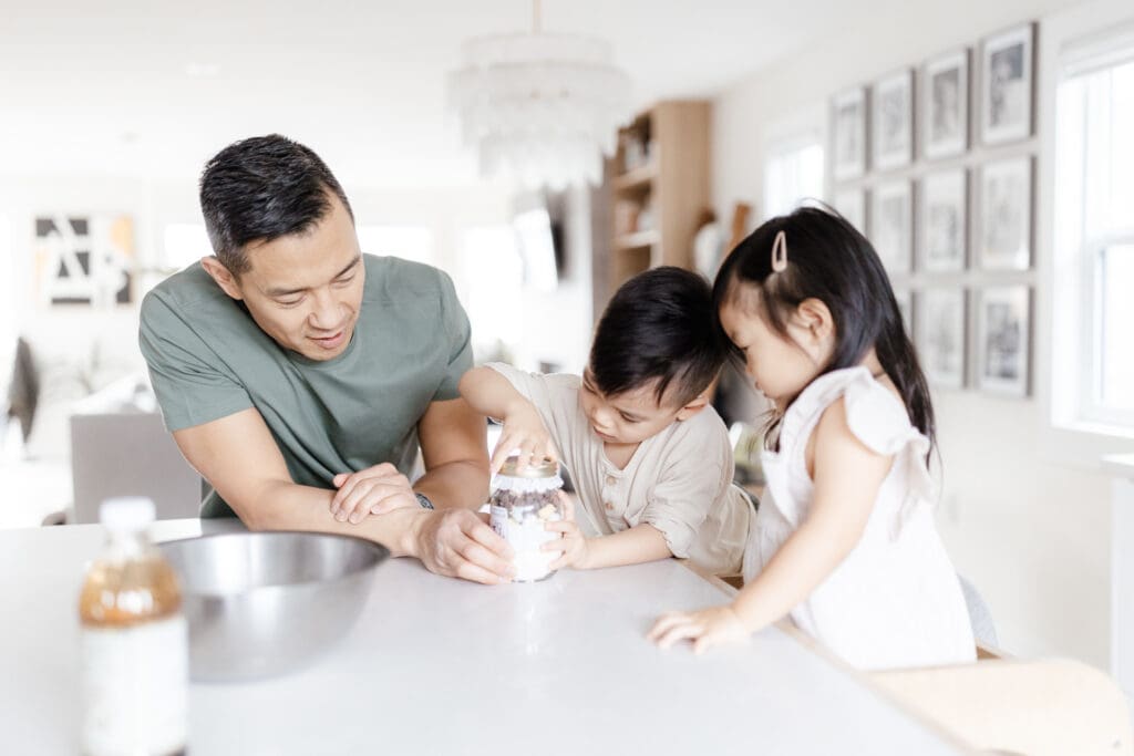 Father and children opening a jar together at the kitchen counter.