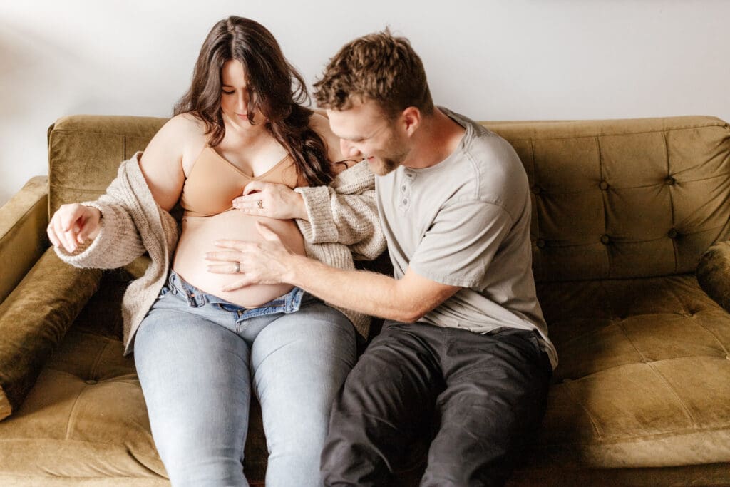 Couple holding baby bump during an in-home maternity session with soft natural light
