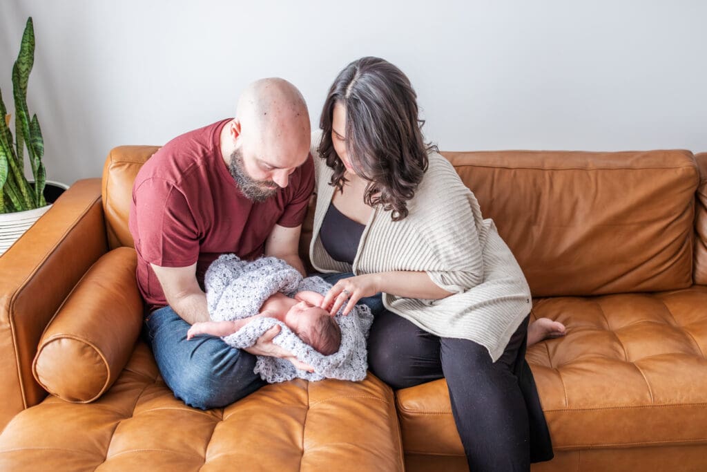 Newborn lying on a soft blanket and parents wearing coordinating outfits during their in-home photo session