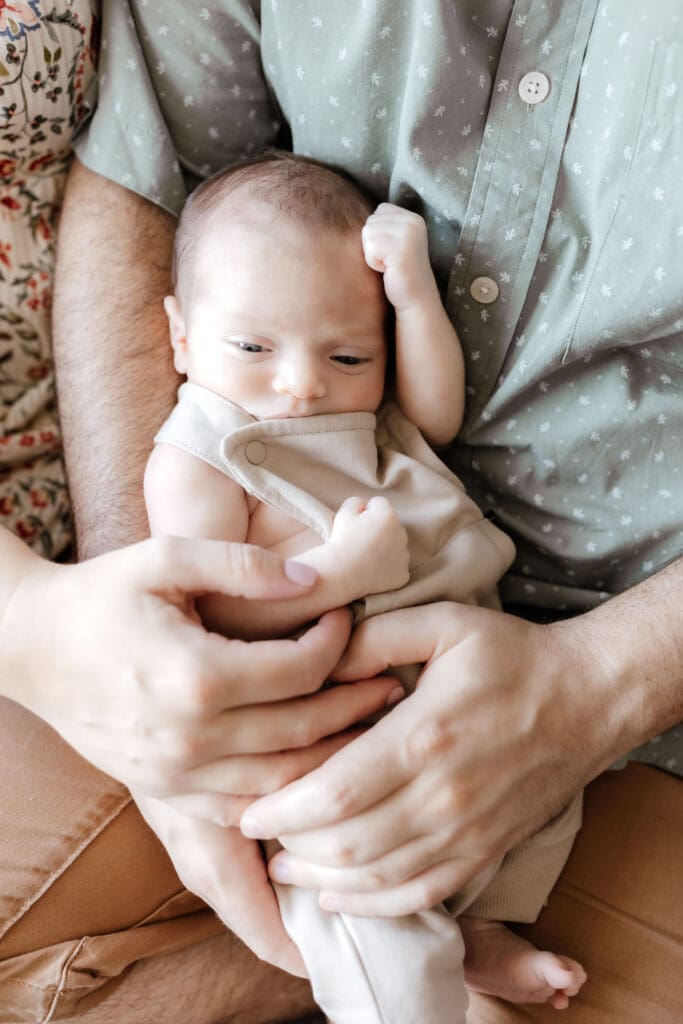 Parent holding sleepy newborn near a window wearing soft neutral tones