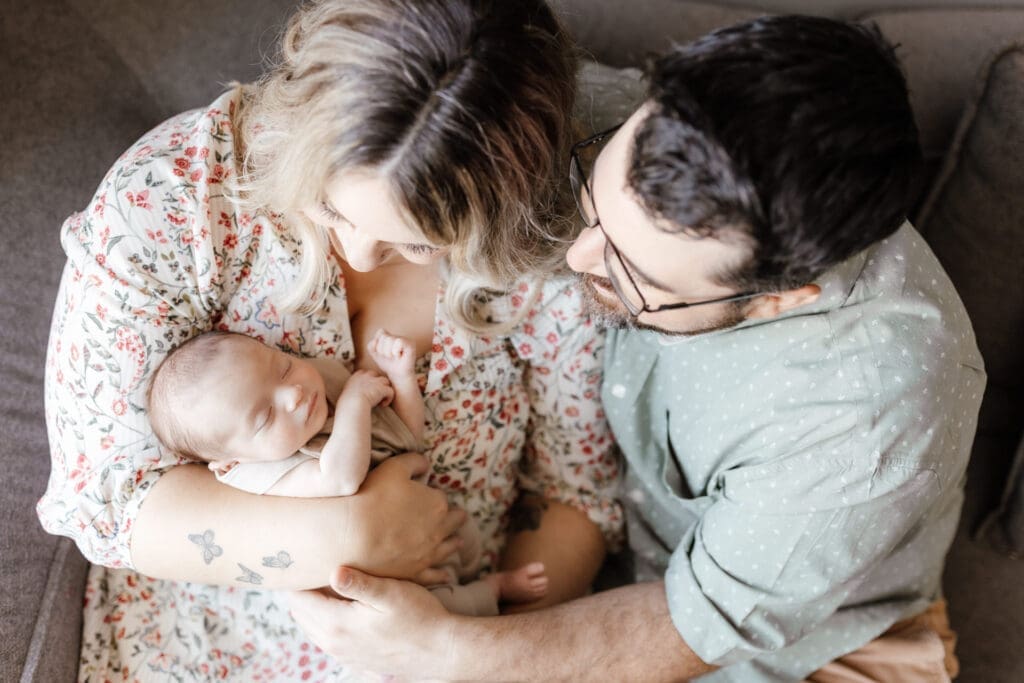 Parents leaning in toward their newborn wearing coordinated neutral clothing
