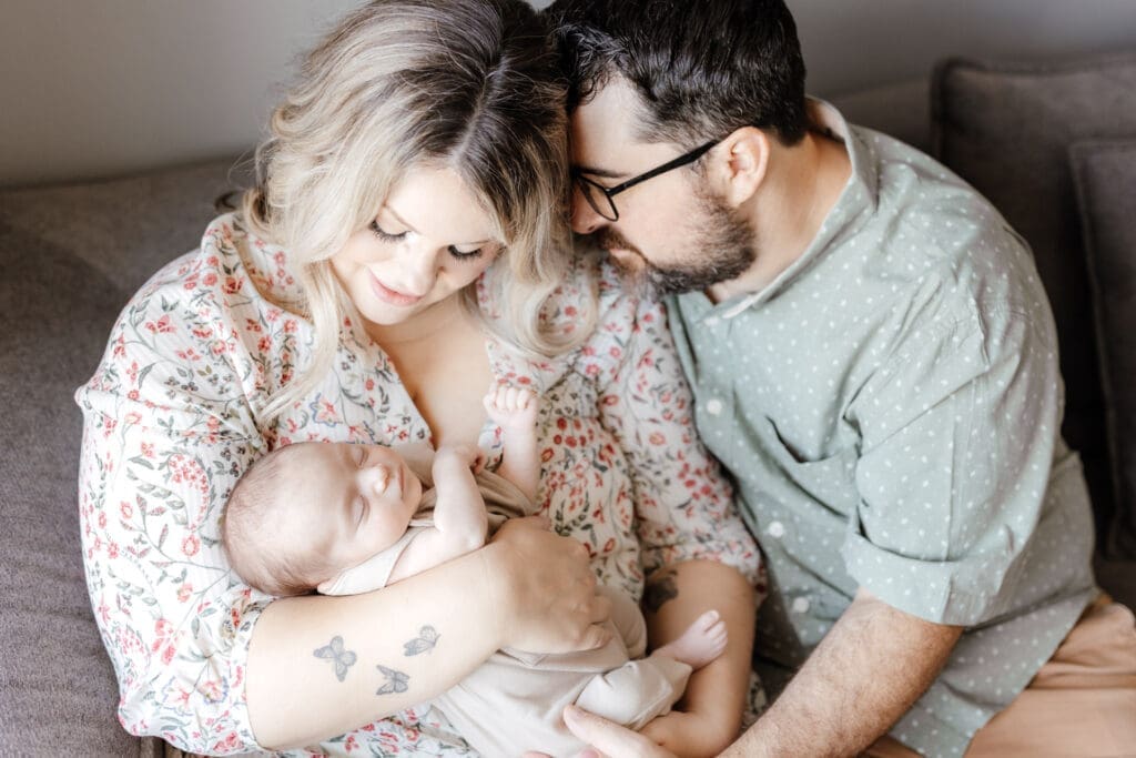 Parents sitting on a sectional couch with newborn and dog