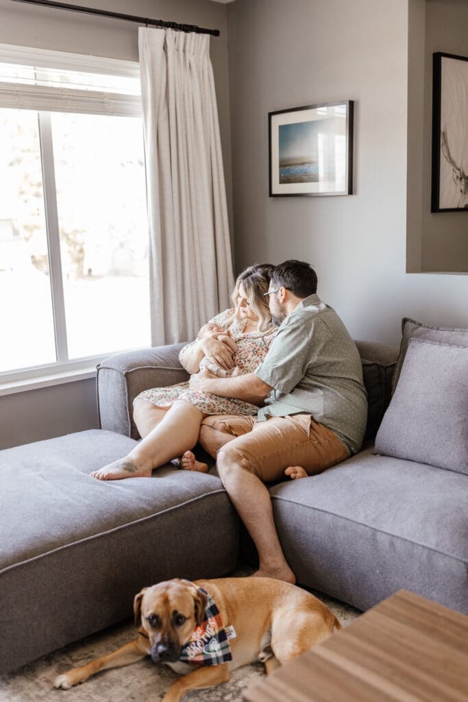 Parents sitting on a sectional couch with newborn and dog
