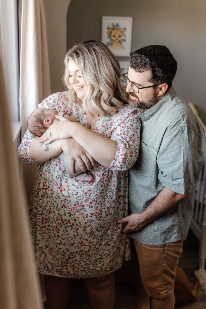 Parents holding newborn together in soft, neutral outfits