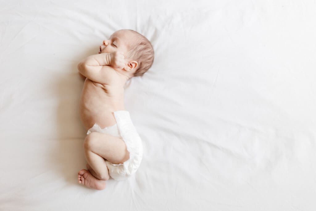 Overhead view of a newborn wearing a diaper stretching on a bed for a light and airy natural look 