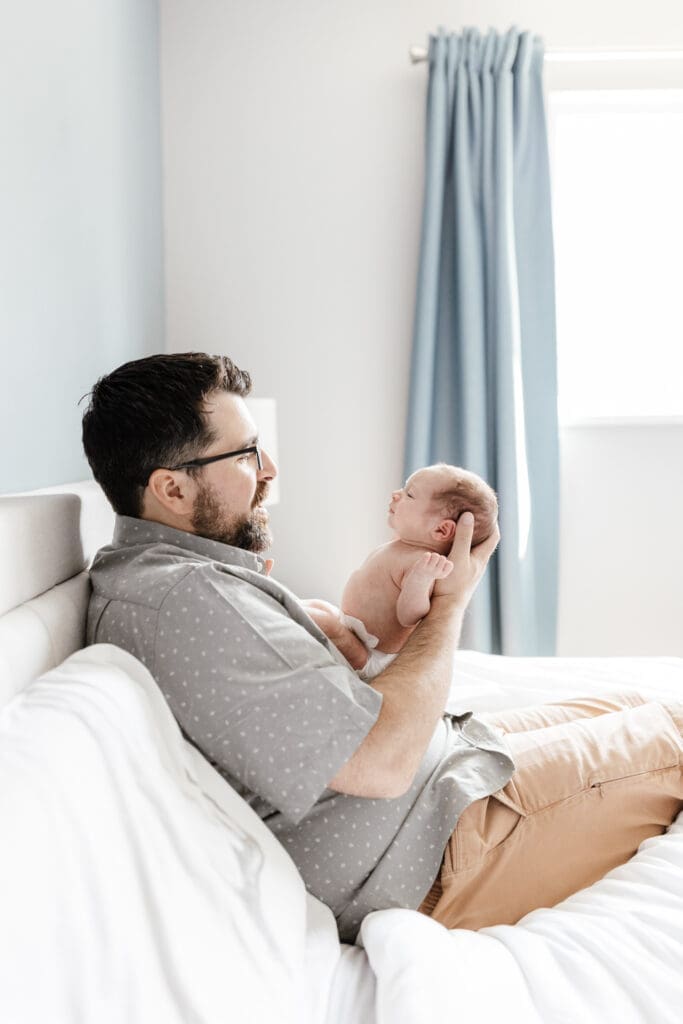 Parent holding newborn upright near a window