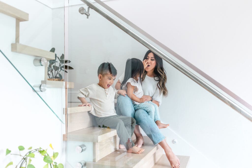 Brother and sister laughing while sitting on the stairs with their mother during an in-home session.