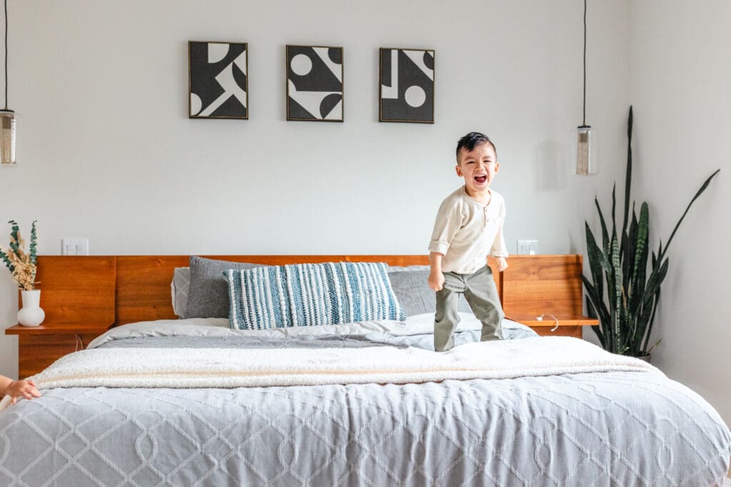 Young boy jumping on bed in in-home lifestyle family photo session showcasing outfit inspiration for boys