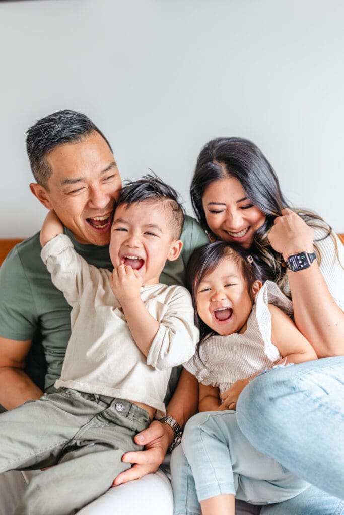 Parents sitting on the bed laughing with their two young children.