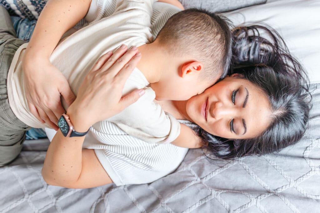 Mother lying on the bed holding her child close in a quiet, tender moment.