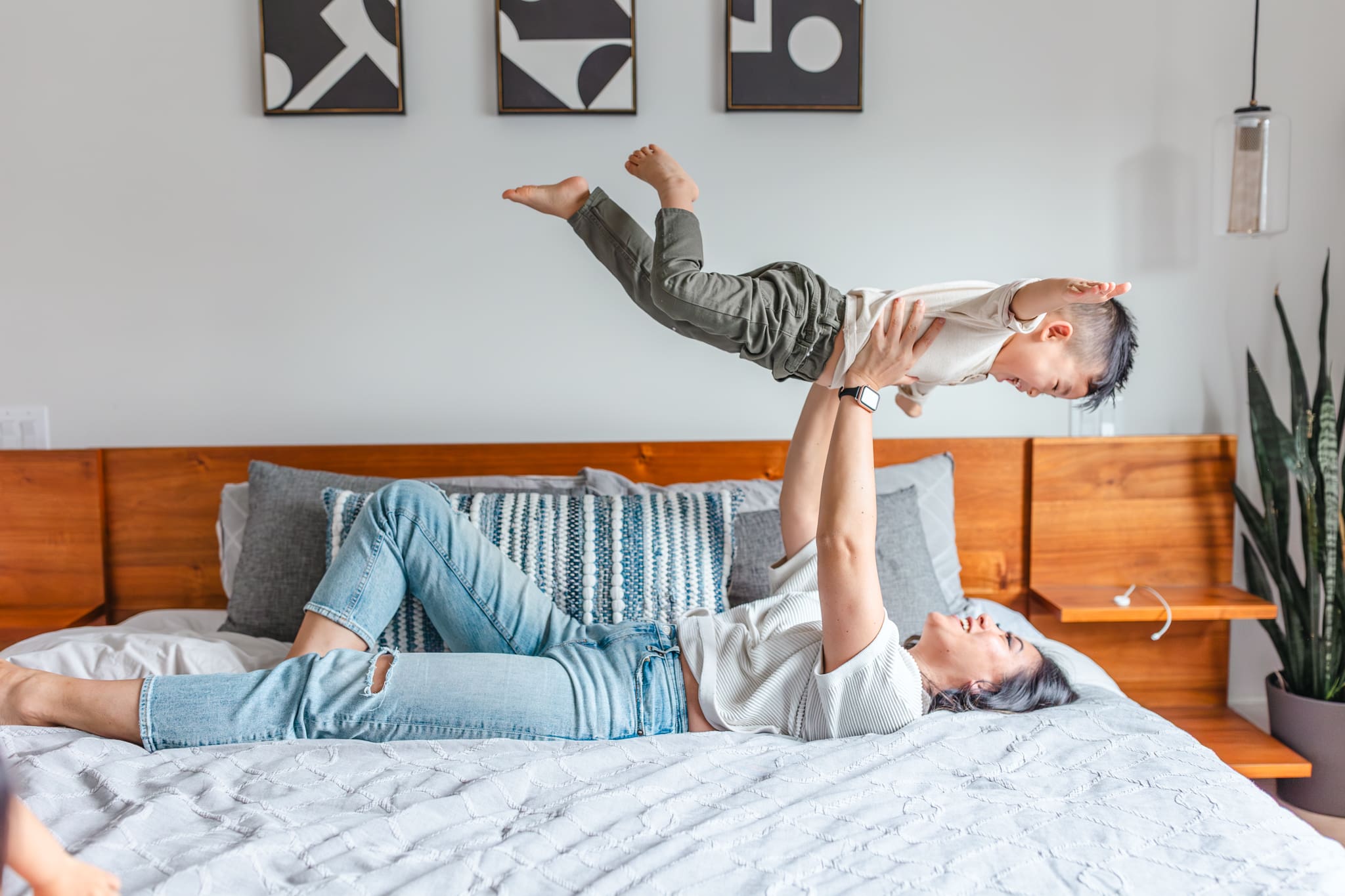 Mother lifting her laughing son into the air on the bed.