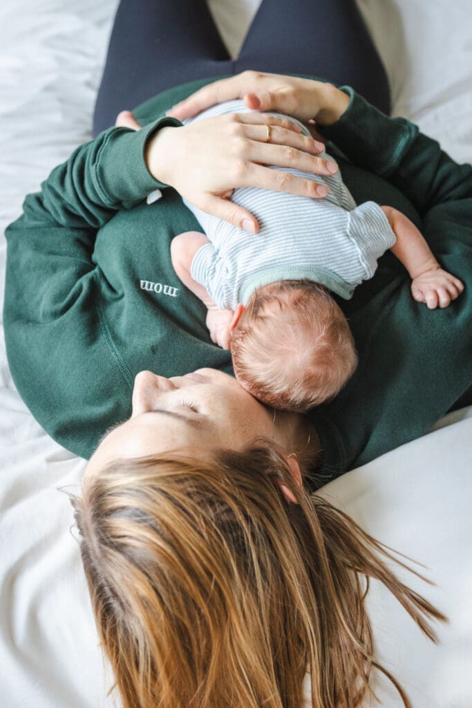 Overhead view of mother holding newborn while laying on the bed in a green sweater during in-home session