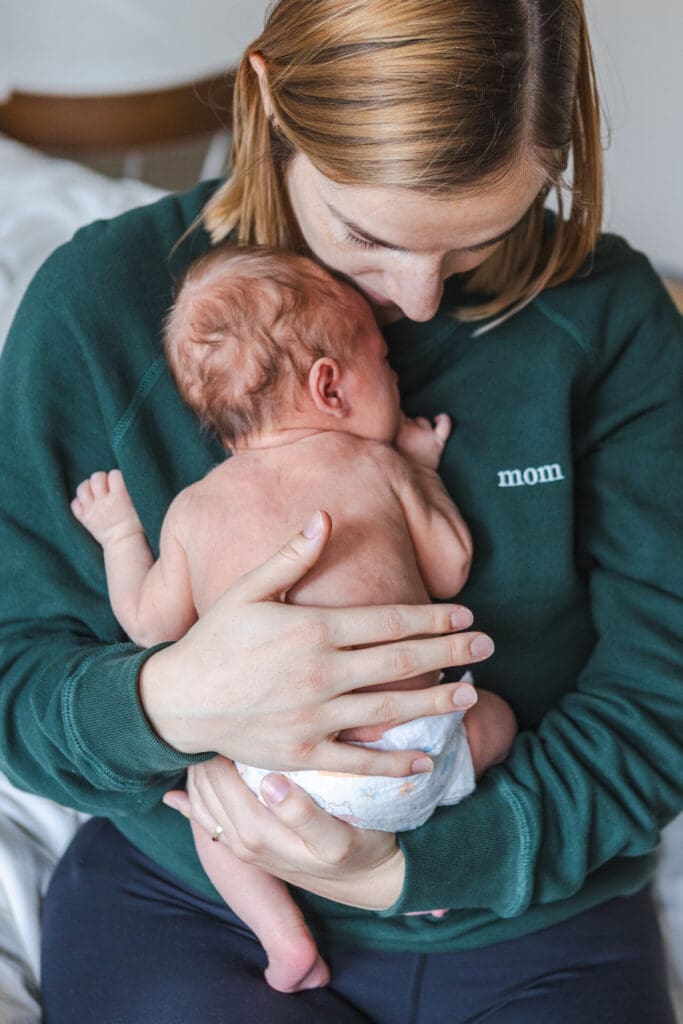newborn wearing only a diaper with mom wearing a green sweater in a natural in-home newborn photoshoot 