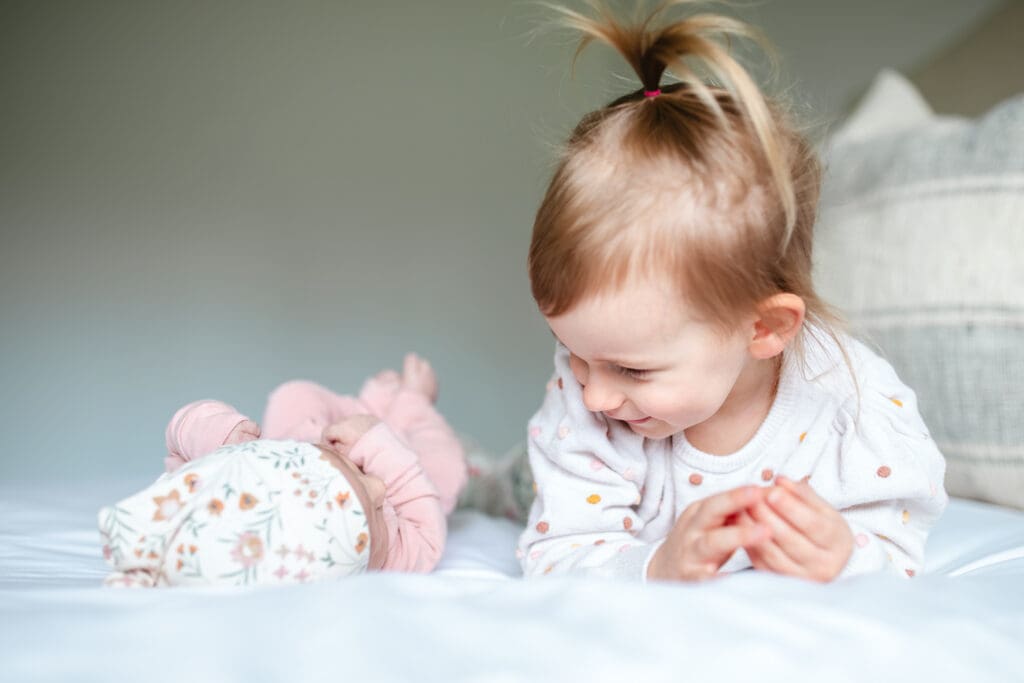 In-home family photo showing toddler with newborn in neutral outfits that work well for lifestyle family photography
