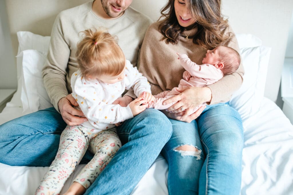 In-home family photo of family sitting on bed with newborn showing neutral outfits that work well for lifestyle family photography
