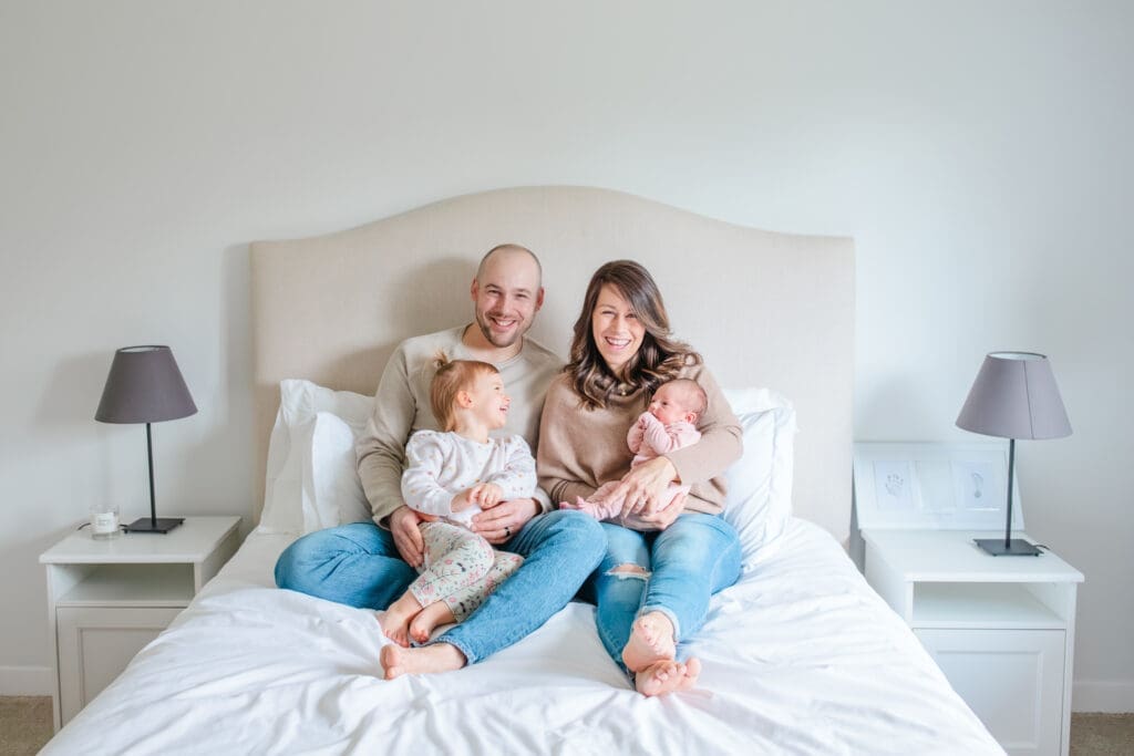 Family smiling and looking at the camera wearing coordinated neutral outfits during an in-home newborn family photography session near Vancouver