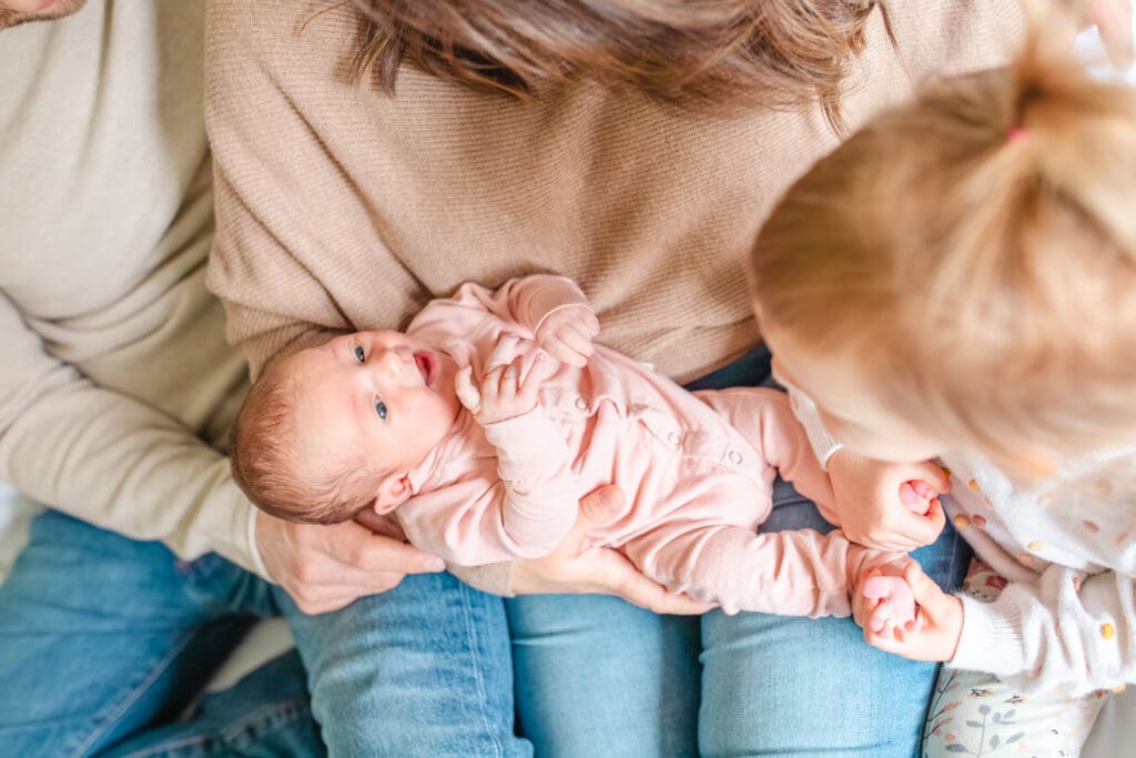 In-home family photo showing toddler counting newborn sister's toes with neutral outfits that work well for lifestyle family photography