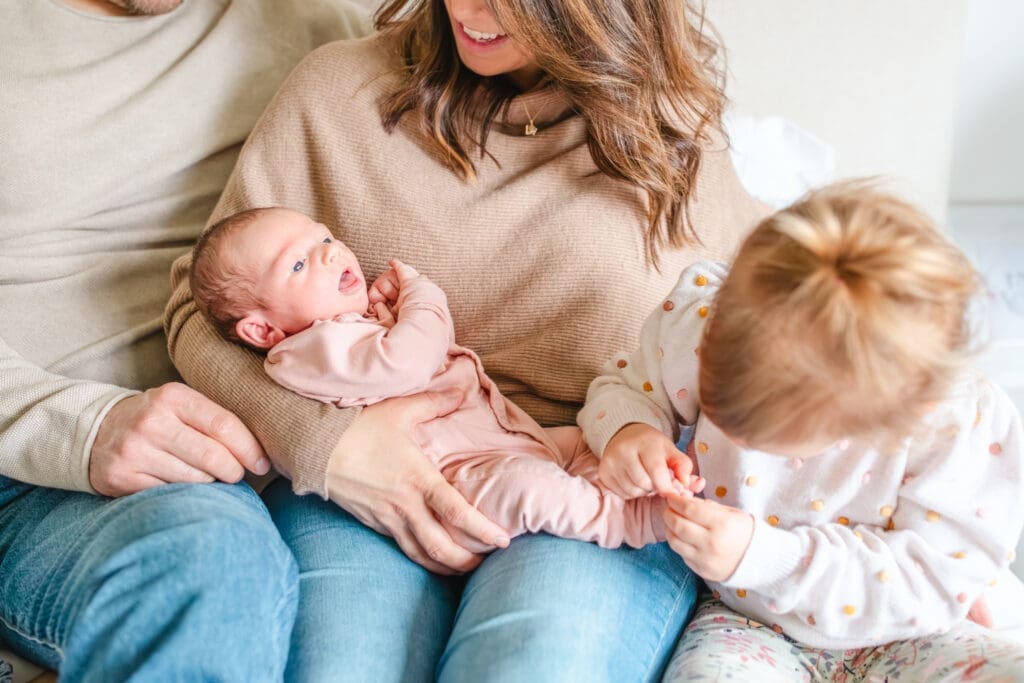 Family wearing coordinated neutral outfits sitting on the bed during an in-home newborn family photography session near Vancouver 