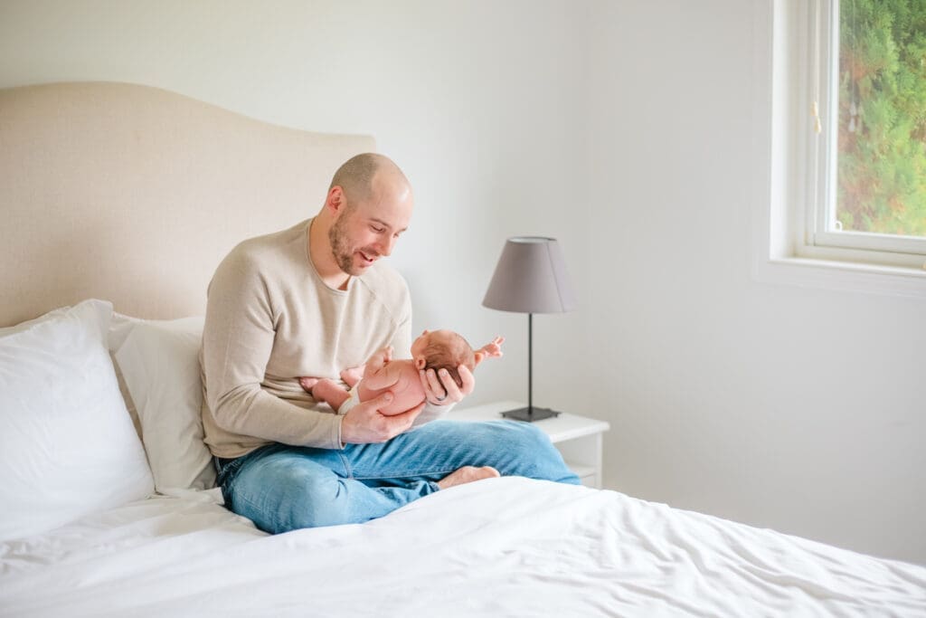 Father and newborn child. Dad is wearing soft neutral outfit with jeans and newborn in a diaper during an in-home family photography session