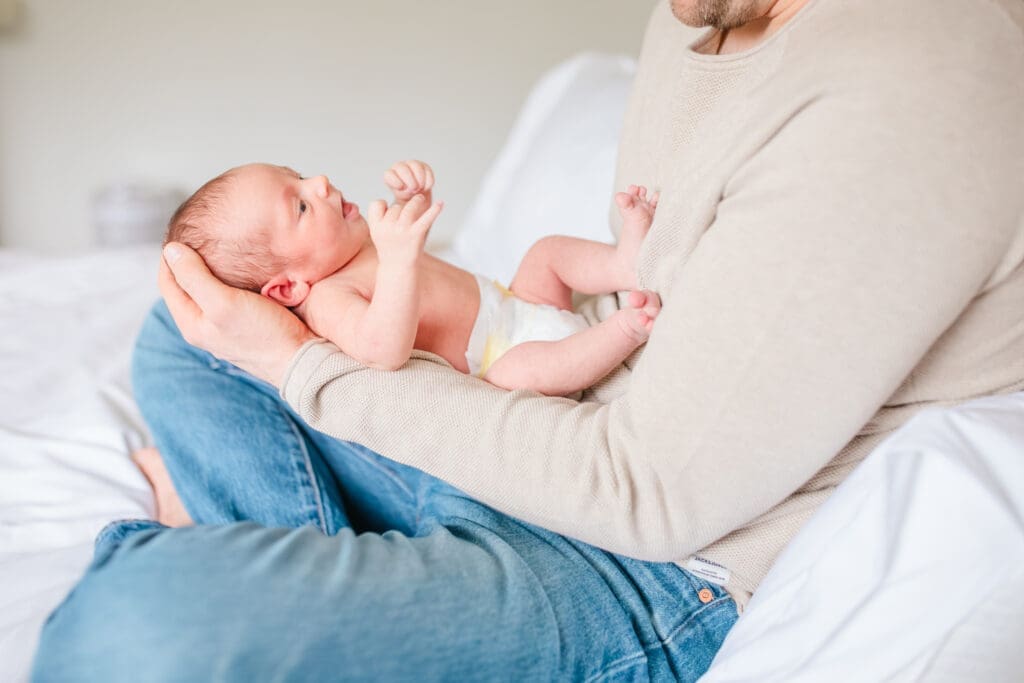 Father and newborn child. Dad is wearing soft neutral outfit with jeans in soft morning light during newborn photo session