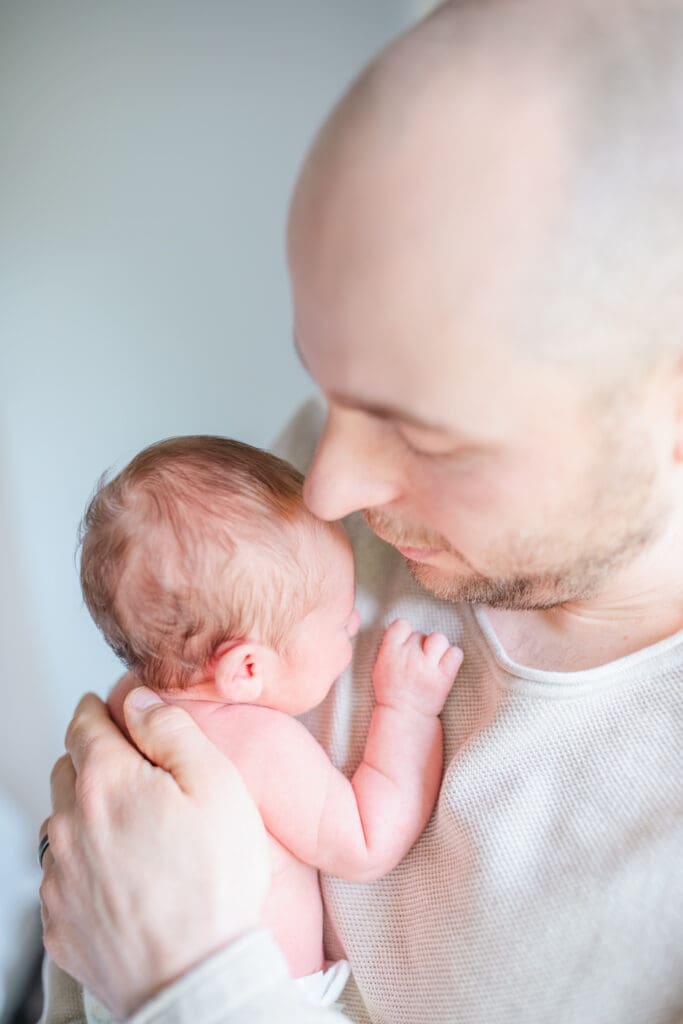 Father tenderly holds his newborn baby girl during a lifestyle newborn session in Vancouver area with Meliza Orellana