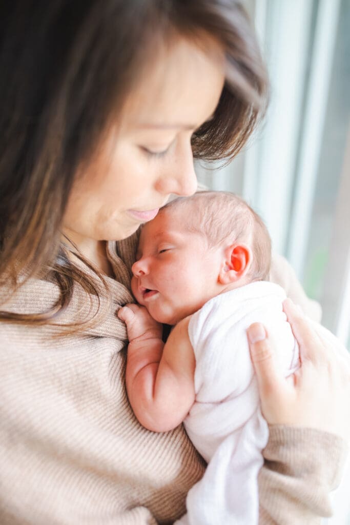 Mother tenderly holds his newborn baby girl during a lifestyle newborn session in Vancouver area with Meliza Orellana