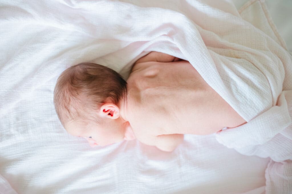 Newborn laying on bed in the soft morning light during lifestyle newborn session with Meliza Orellana