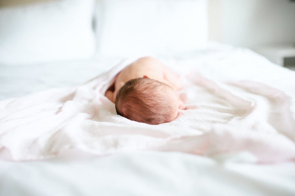 Newborn laying on bed in the soft morning light during lifestyle newborn session with Meliza Orellana