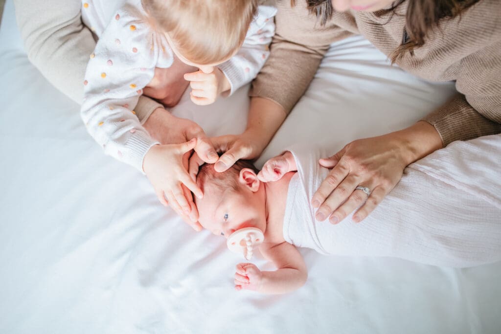 Lifestyle newborn photography with parents and toddler wearing simple, comfortable clothing at home