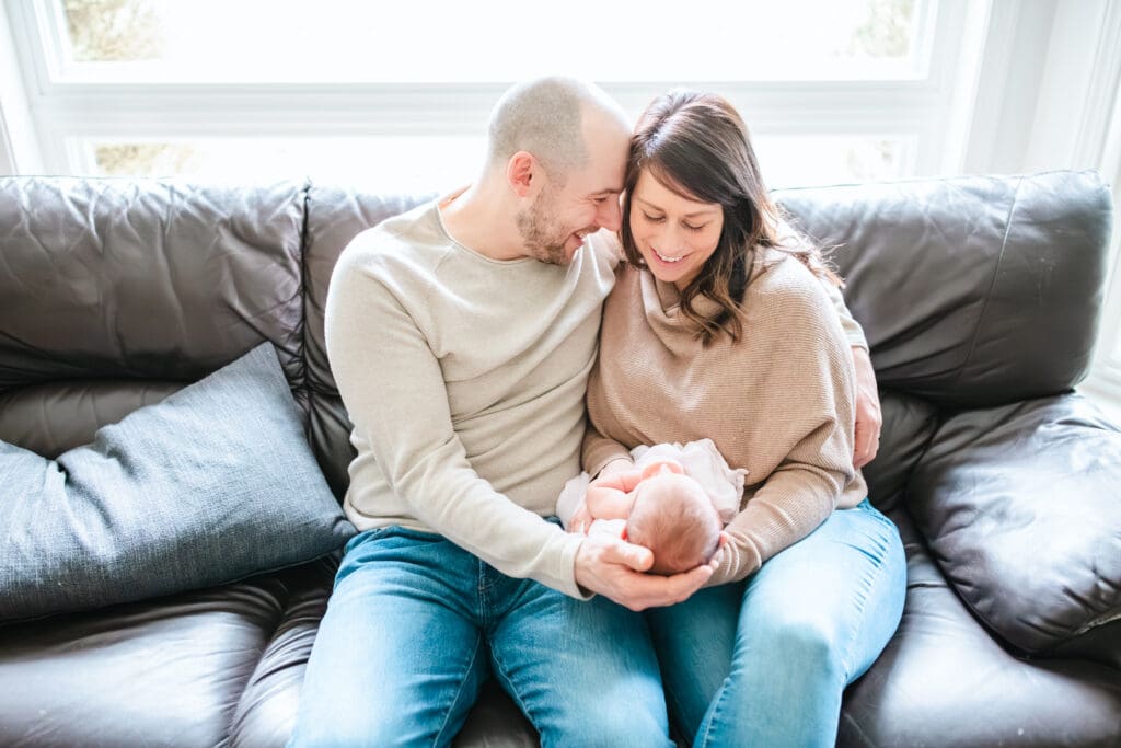 Parents wearing soft neutral tones while sitting on the couch during an in-home newborn photography session
