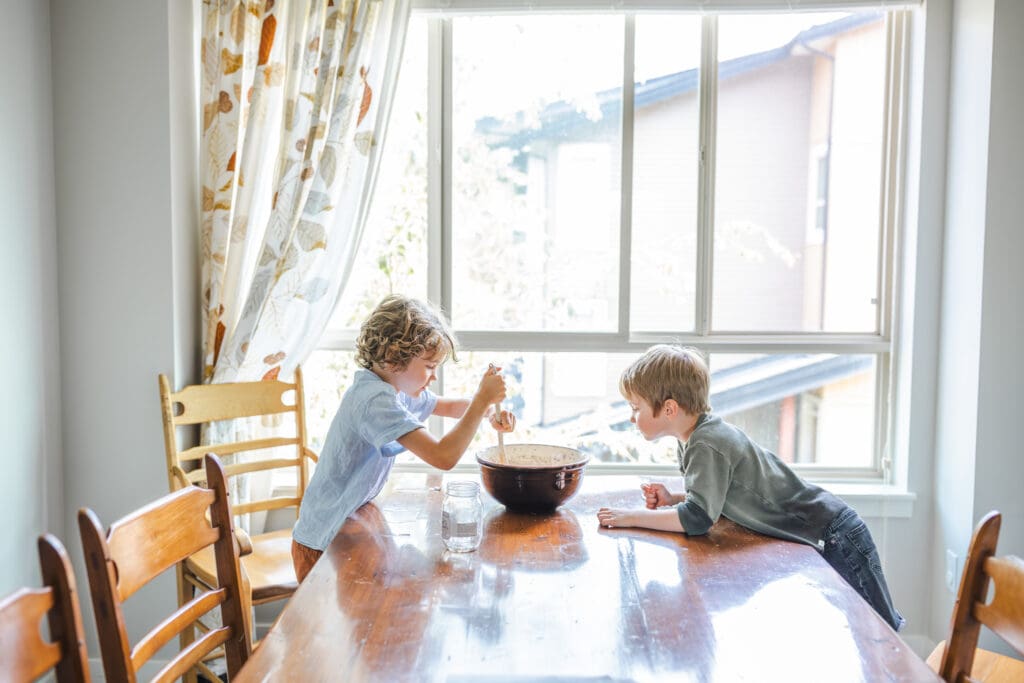 winter window light during in-home family session of brothers baking together in the kitchen