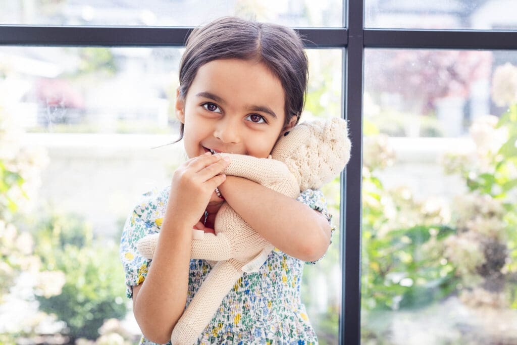 Young child sitting by a window cuddling her stuffie during an in-home family photoshoot in Vancouver.