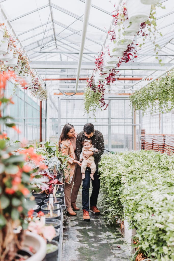 Parents holding their child and sharing a quiet moment during a natural family photo session in a greenhouse